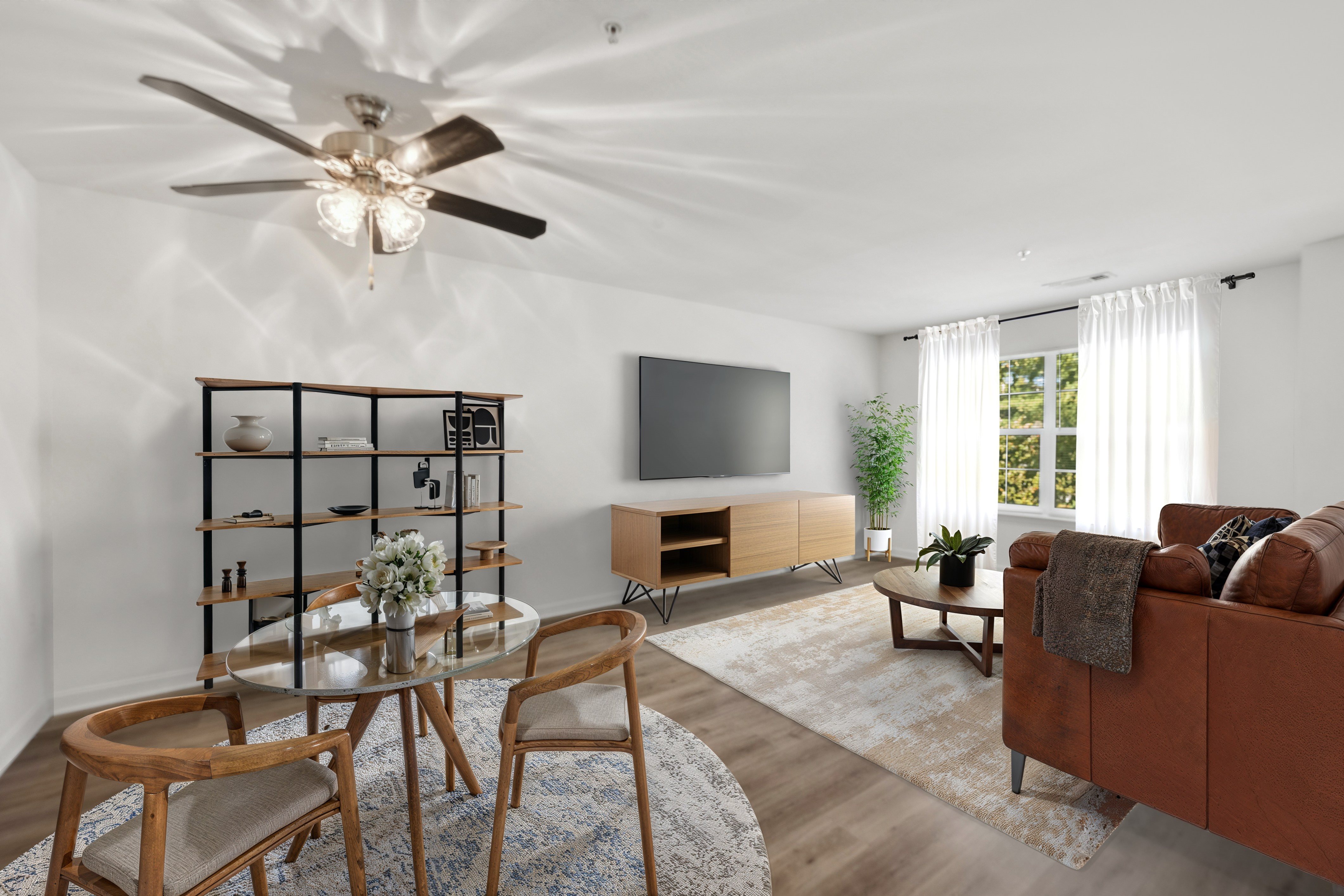 A living room with a brown couch, a glass table, and a ceiling fan.